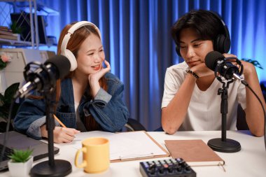 Genç adam ve kadın küçük yayın stüdyosunda mikrofon ve dizüstü bilgisayar kullanarak canlı yayın yapan radyo yayını için röportaj yapacaklar.,