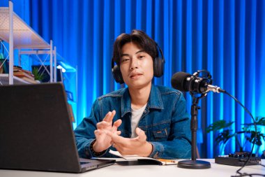 Bilgisayarında kulaklık ve mikroskopla podcast kaydeden bir adam. Parlak stüdyosundan canlı yayın yapan erkek podcaster