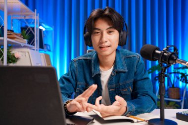 Bilgisayarında kulaklık ve mikroskopla podcast kaydeden bir adam. Parlak stüdyosundan canlı yayın yapan erkek podcaster