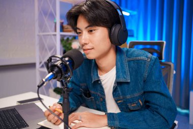 Çalışma alanında kulaklıkla podcast kaydederken mikrofona konuşan odaklanmış genç bir adam..