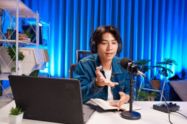 Bilgisayarında kulaklık ve mikroskopla podcast kaydeden bir adam. Parlak stüdyosundan canlı yayın yapan erkek podcaster