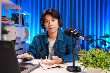 Bilgisayarında kulaklık ve mikroskopla podcast kaydeden bir adam. Parlak stüdyosundan canlı yayın yapan erkek podcaster