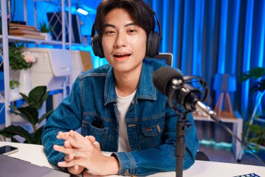 Bilgisayarında kulaklık ve mikroskopla podcast kaydeden bir adam. Parlak stüdyosundan canlı yayın yapan erkek podcaster