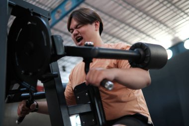 Spor salonundaki ağır antrenman sırasında fazla kilolu bir adam güç antrenmanında mücadele ve kararlılık gösteriyor..