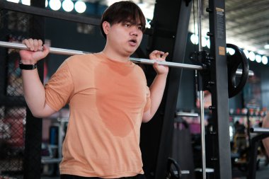 Kilolu bir adam spor salonunda halterle çömeliyor. Güç Eğitimi ve Terleme Çabası