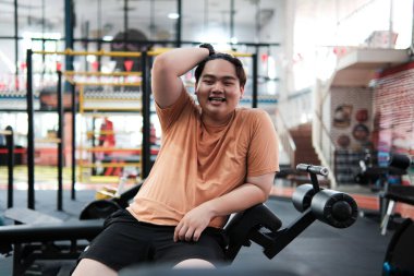 Kilolu adam spor salonunda egzersiz yaptıktan sonra gülümsüyor ve kendinden emin görünüyor. Vücut pozitifliği, kendini kabullenme, motivasyon ve sağlıklı yaşam tarzı kavramı.