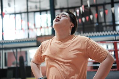 Kilolu bir adam spor salonunda sıkı çalıştıktan sonra yorgun ve soluklanıyor..