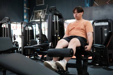 Kilolu bir adam spor salonunda bacak uzatma makinesi üzerinde egzersiz yapıyor. Vücudunun alt kısmına ve dayanıklılığına odaklanıyor..