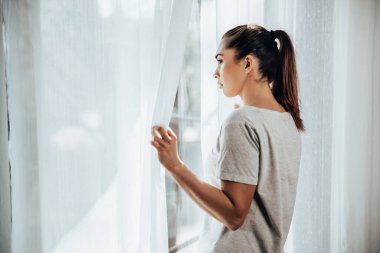 Lonely young girl in depression looking through the window lost in bad pessimistic thoughts.