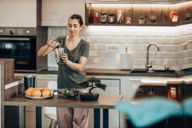 Young woman daydreaming while enjoying morning and preparing a smoothie at home.