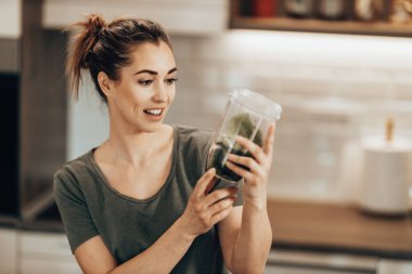 Young woman daydreaming while enjoying morning and preparing a smoothie at home.