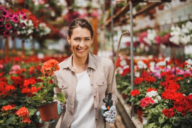 Portrait of a beautiful young woman working in flower greenhouse and looking at camera. Woman entrepreneur.