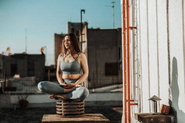 Relaxed woman practicing yoga meditating on a rooftop terrace.