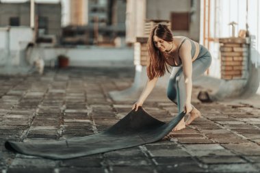Relaxed woman is preparing exercise mat to practicing yoga on a rooftop terrace.