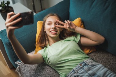 Beautiful teenager girl making selfie with smart phone while having leisure time at her home.