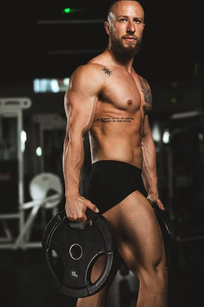 근육질 보디빌더가 헬스클럽에서 웨이트 플레이트를 근육을 보이는 — 스톡 사진