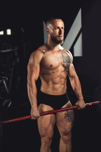 在健身房用杠铃对一个肌肉发达的健美运动员进行了艰苦的训练 — 图库照片