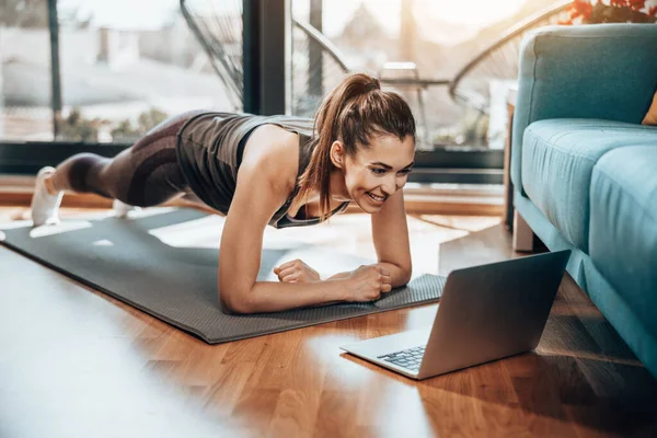 Young Woman Using Laptop While Doing Plank Exercises Home Morning — стоковое фото