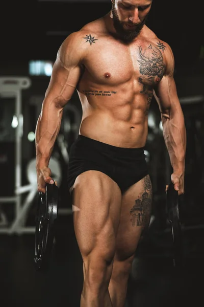 ジムでウェイトプレートで作業した後 彼の完璧な筋肉を示す筋肉のボディビルダーのショット — ストック写真