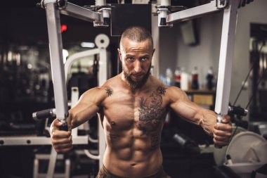 Genç kaslı bir vücut geliştirici spor salonunda göğüs kasları için sıkı antrenman yapıyor..