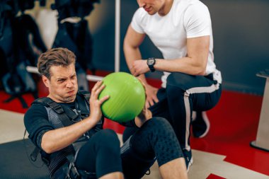 Orta yaşlı bir adam spor salonunda EMS eğitimi sırasında mekik egzersizleri yapıyor..