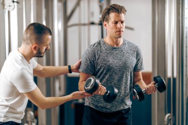 Orta yaşlı bir adam spor salonunda kişisel antrenörüyle antrenman yapıyor..