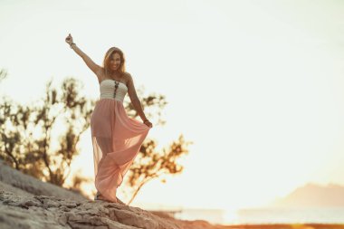 An attractive young woman is having fun and dancing while enjoying a summer vacation at the seaside.