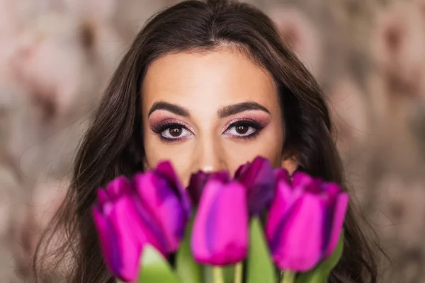 紫色のチューリップの花束を持っていると彼女の顔に素敵なメイクを表す美しい目を持つ魅力的な若い女性の肖像画 — ストック写真