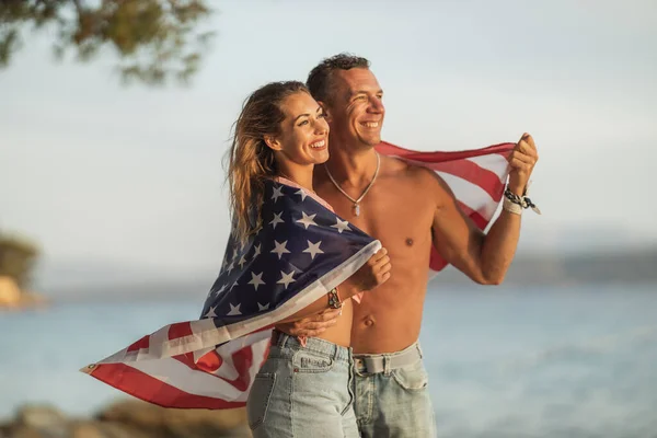一对挂着美国国旗 面带微笑的夫妇在海滩上享受着悠闲的一天 — 图库照片