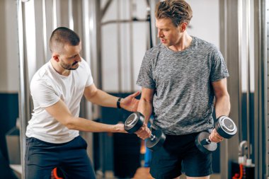 Orta yaşlı bir adam spor salonunda kişisel antrenörüyle antrenman yapıyor..