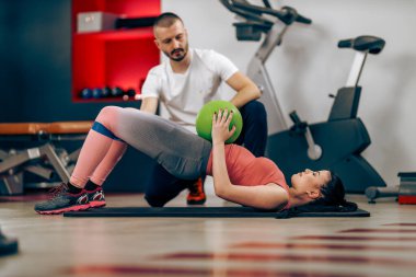 Young woman is doing training for abs with personal trainer in a gym.