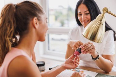 Güzellik uzmanının karşısında oturan ve güzellik salonunda tırnak rengini seçen genç bir kadın..