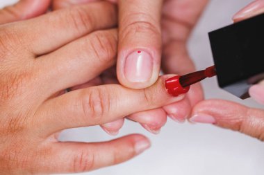 Bir güzellik salonunda manikür yaparken kırmızı oje sürerken tanınmayan bir güzellik uzmanının kesilmiş görüntüsü..