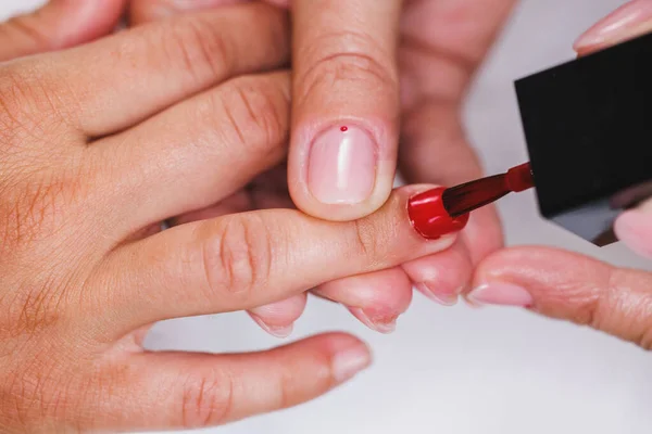 stock image Cropped image of an unrecognizable beautician applying red nails polish to woman during manicure treatment in a beauty salon.