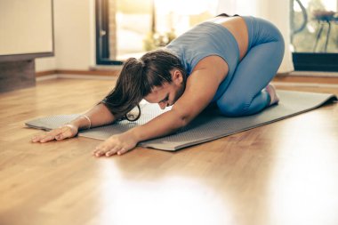 Sabahları evde egzersiz yapan genç bir kadın. Egzersiz minderinde esneme egzersizi yapıyor..