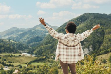 Kollarını açmış, doğada duran ve temiz havanın tadını çıkaran siyah bir kadının arka görüntüsü..