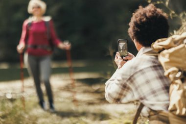 Yürüyüş sırasında birbirlerinin akıllı telefonlarıyla fotoğraf çeken iki melez bayan arkadaş..