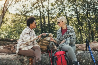 Doğada yürüyüş yapan iki melez kız arkadaş güneşli bir sonbahar gününde çay molası veriyorlar..