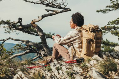 Yetişkin siyah kadın dağ yamacında otururken manzaranın tadını çıkarıyor..