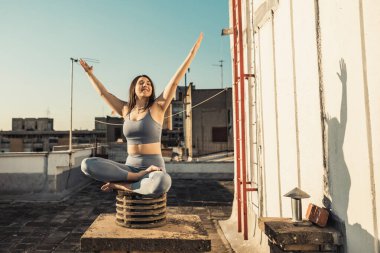 Relaxed woman practicing yoga meditating on a rooftop terrace.