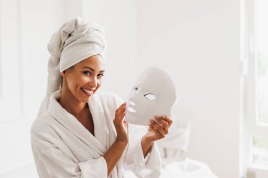 Güzel genç bir kadın güzellik salonunda yüzü için öncü ışık terapisi maskesi yaptırıyor..