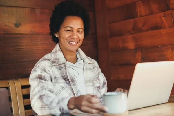 Černá Žena Pracuje Notebooku Zatímco Tráví Dovolenou Útulném Dřevěném Domě — Stock fotografie