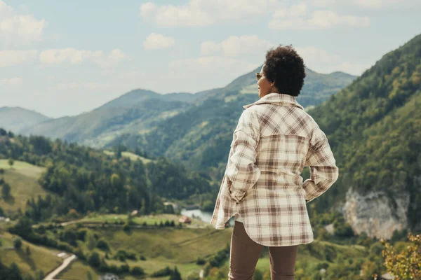 Rear view of a black woman standing in nature and enjoying fresh air on mountain in a sunny day.