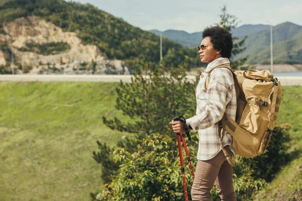 美しい晴れた秋の日に山の中で一人でハイキングバックパックやトレッキングポール付きの成熟した黒人女性 — ストック写真