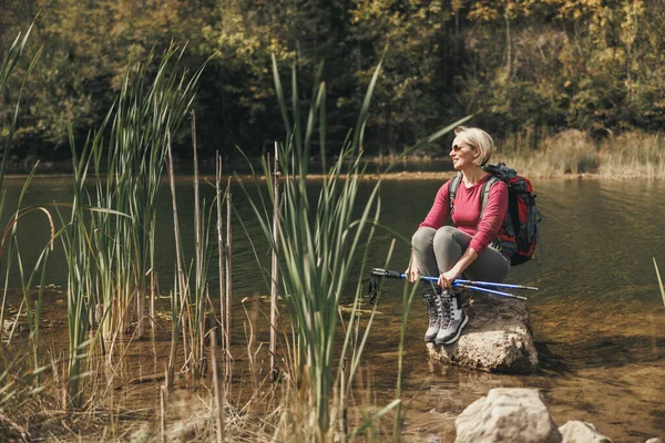 バックパック付きの女性ハイカーは岩の上に一人で座って 山の中で湖の景色を楽しんでいます — ストック写真