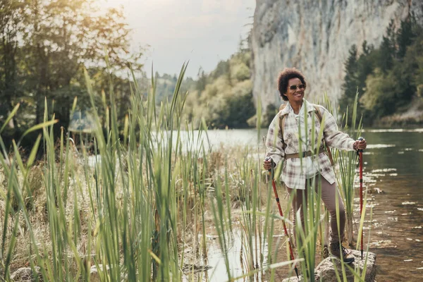 Mature black woman with backpack enjoying the view of lake and relaxing during hiking in mountain.