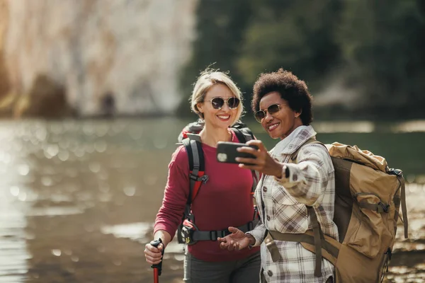 Duas Amigas Mestiças Tirando Selfies Por Lago Durante Uma Caminhada — Fotografia de Stock