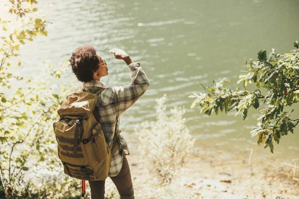 Mature black woman with backpack taking a break and enjoying the view of lake while hiking.