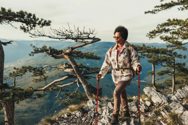 Olgun siyahi kadın bir tepenin üstünde duruyor ve dağlardaki yürüyüşü sırasında manzaranın tadını çıkarıyor..