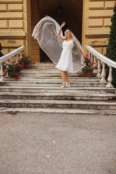 美丽的新娘在户外欢欢喜喜地跳下楼梯 而新娘的婚纱在空中飘扬 — 图库照片